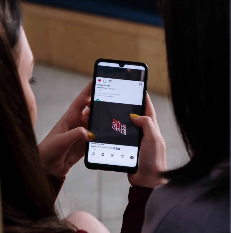 ragazza che guarda i social al telefono con l'amica accanto